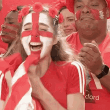 a woman with a cross painted on her face is standing in a crowd of people wearing red shirts .