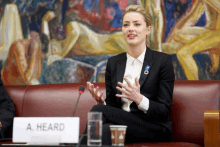 a woman in a suit sits at a table with a sign that says a heard