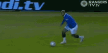 a soccer player is kicking a ball in front of an advertisement for rangers tv