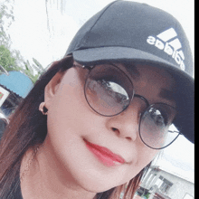 a woman wearing a black adidas hat and sunglasses smiles for the camera