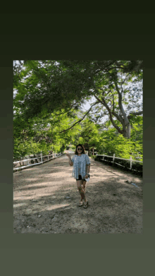 a woman is standing on a dirt road under trees