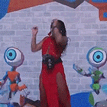 a woman in a red dress is standing in front of a brick wall surrounded by eyeballs .