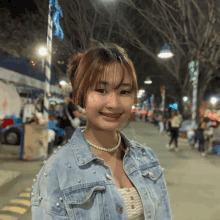 a woman wearing a pearl necklace and a denim jacket smiles