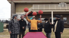 a group of men are standing around a table holding basketballs in front of a building that says " awesome "