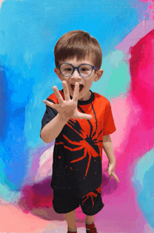 a young boy wearing glasses and a spider shirt makes a funny face