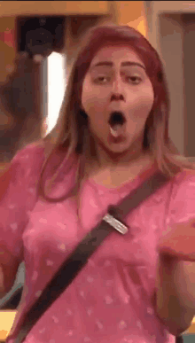 a woman in a pink shirt is making a funny face while standing in a room .