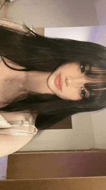 a girl with long black hair and bangs is taking a selfie in a room .