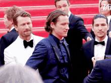 a group of men in tuxedos and bow ties are standing on a red carpet with a variety logo in the background