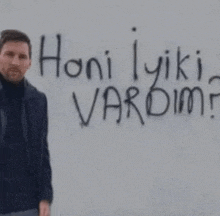 a man is standing in front of a wall with graffiti on it that says `` honi iyiki vardim '' .