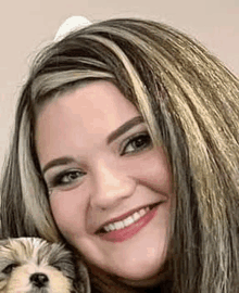 a woman is smiling while holding a small dog and looking at the camera .