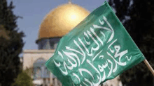 a green flag with arabic writing on it is flying in front of a mosque .