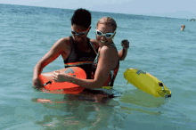 a man and a woman are swimming in the ocean and the woman is wearing a rainbow tank top with the word coe on it