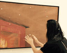 a woman touches a painting of a fireplace