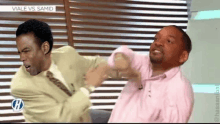 a man in a suit and tie is fighting another man in a pink shirt on a television show .