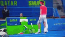 a man in a red shirt is holding a tennis racquet on a tennis court in front of a sign that says qatar