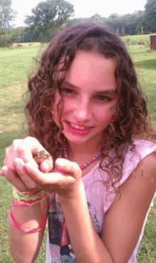 a girl with curly hair holds a small frog in her hands