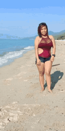 a woman in a red swimsuit stands on a sandy beach