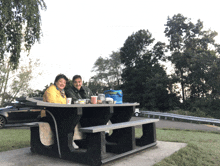 a man and woman sit at a picnic table with a blue cooler in the background