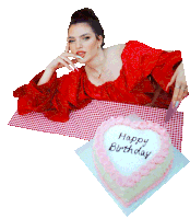 a woman in a red dress sits at a table next to a heart shaped cake that says happy birthday