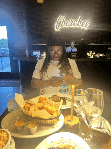 a woman sits at a table in front of a neon sign that reads cherokee