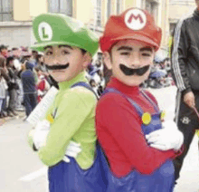 two young boys dressed up as mario and luigi are standing next to each other on a street .