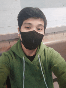 a man wearing a green hoodie and a black face mask takes a selfie