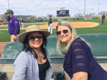 two women are sitting in the dugout at a baseball game and one has a hat on