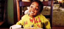 a young boy in a yellow shirt is sitting at a table with a plate of food and a cup of coffee .