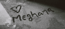 the name meghana is written on a black surface with a heart