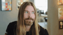 a man with long hair and a beard is making a funny face in a room .