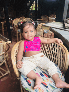 a little girl sits in a wicker chair with a feather cushion