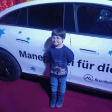 a young boy stands in front of a car that says manes for die