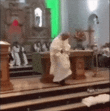 a priest is kneeling down in front of a podium in a church with a green light behind him .