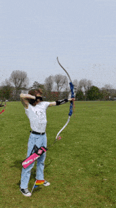 a person is holding a bow and arrow in a field with a pink bag that says ' why ' on it