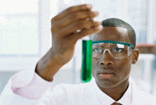 a man wearing safety goggles looks at a test tube with green liquid in it