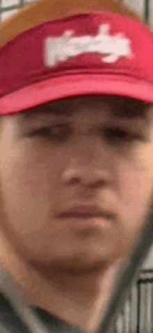 a close up of a man wearing a red hat with a white logo on it .