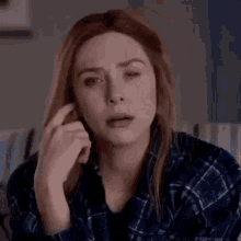 elizabeth olsen is wearing a plaid shirt and making a funny face while talking on a cell phone .