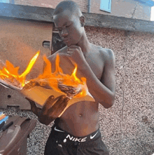 a shirtless man wearing nike shorts is holding a piece of paper on fire