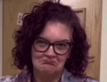 a woman with curly hair wearing glasses is making a funny face .