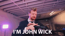 a man in a suit and tie is holding a gun and says " i 'm john wick "