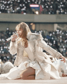 a woman singing into a microphone while wearing a white coat that says ' taylor swift ' on it