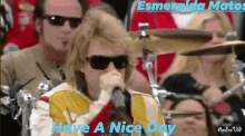 a man wearing sunglasses singing into a microphone with the words have a nice day behind him