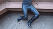 a person wearing black pants and black boots sits on a wooden deck