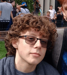 a young man with curly hair wearing glasses looks at the camera