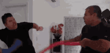 two men are fighting each other in a living room while holding a red ribbon .