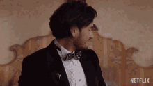 a man in a tuxedo and bow tie is sitting in front of a bed with a netflix logo in the corner