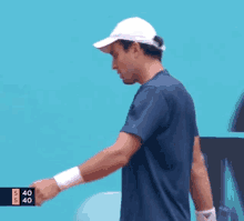 a man wearing a white hat and a blue shirt is standing in front of a blue wall with a scoreboard that says 540