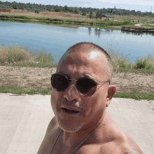 a shirtless man wearing sunglasses is standing in front of a body of water