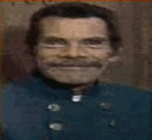 a close up of a man with a mustache smiling in a blurry photo .