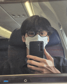 a man wearing glasses and a face mask is taking a selfie on an airplane